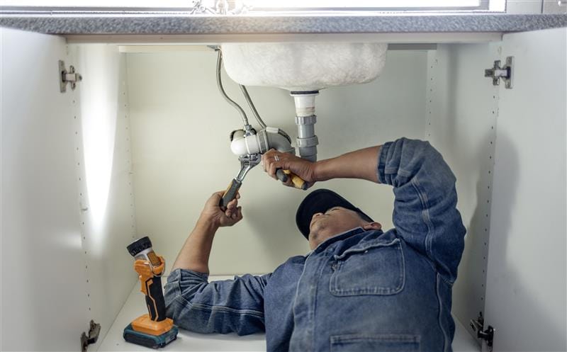 Plumber repairing pipes beneath a bathroom sink in Moorpark